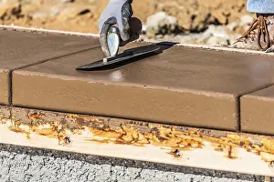 Construction Manpower Drucke: Construction worker using trowel on wet cement forming coping around new pool