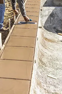 New Construction Site Drucke: Construction worker using trowel on wet cement forming coping around new pool