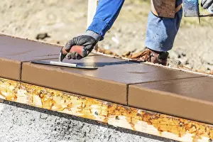 Construction Industry Workforce Drucke: Construction worker using trowel on wet cement forming coping around new pool