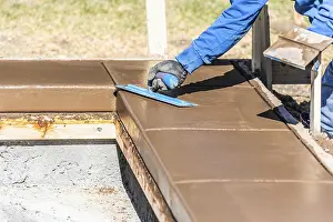 Building Construction Site Drucke: Construction worker using trowel on wet cement forming coping around new pool