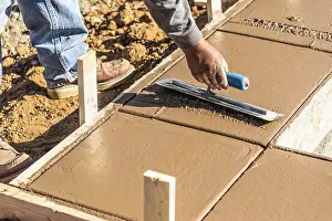 Construction Industry Workforce Drucke: Construction worker using trowel on wet cement forming coping around new pool