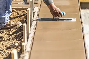 New Pool Construction Drucke: Construction worker using trowel on wet cement forming coping around new pool