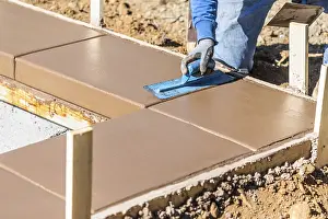 Swimming Pool Building Drucke: Construction worker using trowel on wet cement forming coping around new pool