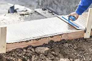 New Construction Site Drucke: Construction worker using trowel on wet cement forming coping around new pool