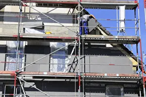 Construction Site Management Drucke: Construction workers insulate a house facade