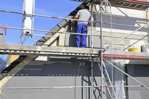 Construction Site Workman Drucke: Construction workers insulate a house facade