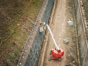 Construction Work In Southern Germany Drucke: Construction workers on a lift attach a net to a steep slope