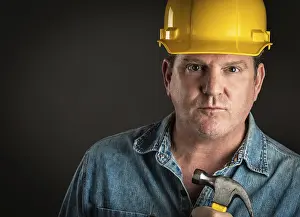 Man In Hard Hat Drucke: Serious contractor in hard hat holding hammer with dramatic lighting