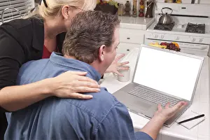 Couple In Kitchen Drucke: Couple in kitchen using laptop with blank screen