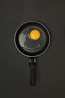 Studio Shot Of Egg Drucke: Cracked egg in pan, dark background