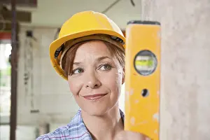 Female Construction Worker Drucke: Craftswoman with hard hat checking with a level