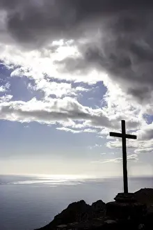 Uninhabited Rocky Shore Drucke: Cross on a cliff with storm clouds
