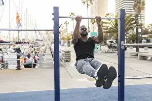 Pull Up Bar Workout Drucke: A cuban man performs exercises on a pull up bar by a marina