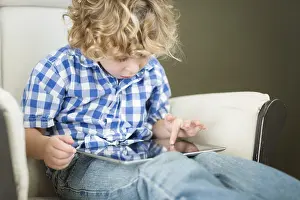 Tablet Computer Use Drucke: Cute young blond boy using his computer tablet in a chair