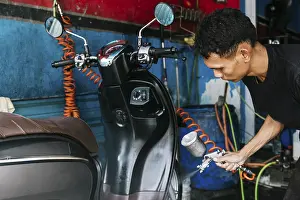 Cleanliness Importance Drucke: A dedicated worker cleans a motorcycle using a sprayer in a vibrant workshop setting