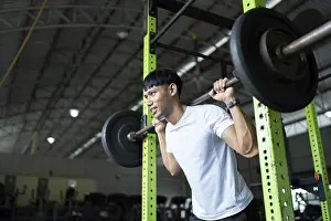 Bodybuilding Exercises Drucke: A determined young man performs squats with a barbell