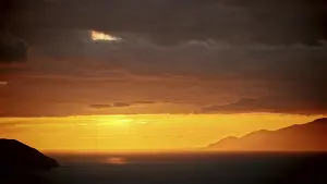 Orange Colored Evening Sky Drucke: A dramatic bright orange sunset behind the mountains with dark clouds