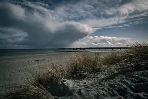 German Federal Republic Coastal Scenery Drucke: Dramatic cloud formations over a beach with a long pier in the background