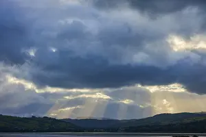 Dramatic Mountain Landscape Drucke: Dramatic sky with rays of light breaking through the clouds over a mountainous landscape