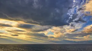 Cloudy Atmospheric Images Drucke: Dramatic sky over the sea with sun rays breaking through the clouds