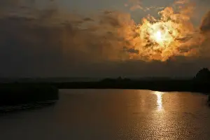 Dramatic Evening Sky Drucke: Dramatic sunset behind clouds over a quiet river with golden reflection