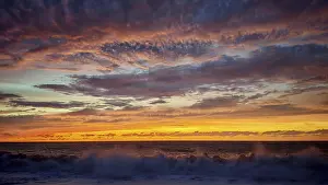 Atmospheric Light Of The Setting Sun Drucke: Dramatic sunset with powerful cloud formations and breaking waves in the foreground