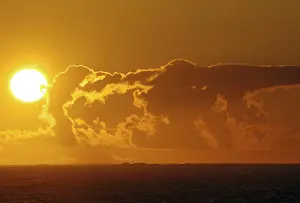 Atmospheric Light Of The Setting Sun Drucke: A dramatic sunset over the sea with bright orange clouds