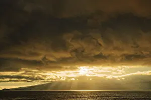 Warm Light Of The Setting Sun Drucke: Dramatic sunset with sun rays breaking through the clouds over the sea