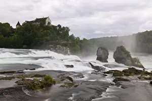 Swiss Tourist Attraction Drucke: Dramatic waterfall flows past rocks to a castle