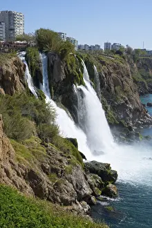 Western Asia Landscapes Drucke: Dynamic waterfall flows into the sea surrounded by rocks and cityscape in the background