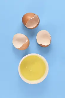 Healthy Eating Protein Source Drucke: Egg white in bowl next to broken eggshells on yellow background