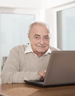 Man Smiling At Camera Drucke: Elderly man using a PC