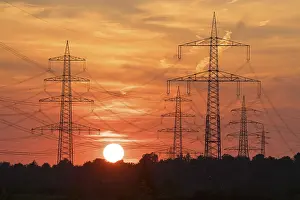Electricity Supply Infrastructure Drucke: Electric masts in front of a dramatic sunset with orange sky and clouds in the background