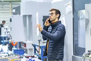 Communicative Young Adult Man Drucke: Engineer talking to the mobile in a computer numeric control factory