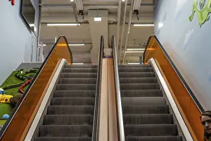 Bilder Datiert 13. April 2024: Oberseite einer Rolltreppe mit orangefarbenen Glasabsperrungen.