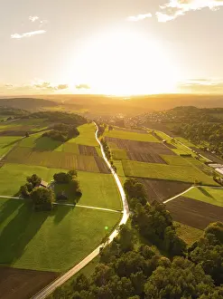 Black Forest Sunset Drucke: Extensive fields and trees in the glowing red light of the sunset with reflecting sunlight