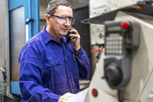 Industrial Building Inspection Drucke: Factory worker operator in the numerical control sector talking on the phone with a client