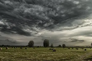 Cloudy Weather Europe Drucke: Field of hay bales in Romagna in Italy under dark clouds