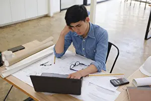Building Architecture Plans Drucke: A focused architect and engineer using a laptop to work on blueprints