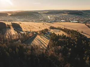 Calw District Scenery Drucke: Forests and fields with a town in the background at sunrise