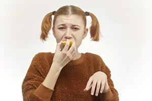 Facial Expression Photography Drucke: Fun girl eats lemon on white background, grimacing