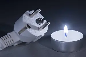 Power Failure Concept Drucke: Glowing candle next to electrical plug in cold light