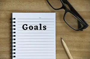 Wooden Table Background Drucke: Goals text on notepad with glasses