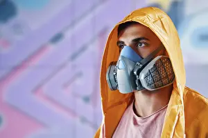 Straßenkünstler Drucke: Spraymaler in Atemschutzmaske steht nahe der Wand mit seinen farbenfrohen Bildern mit Auslassraum