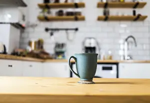 Deserted Kitchen Table Scene Drucke: Green coffee cup on kitchen table blurred kitchen in background