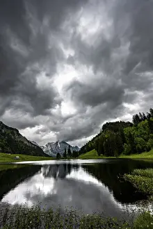 Empty Countryside Landscapes Drucke: Groppelensee with reflection of the Altmann summit in the background under a threatening cloudy sky