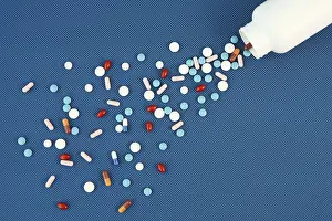 Blue Background Pills Drucke: Group of assorted tablets and Capsules spilling out of white bottle