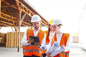 Construction Plan Blueprint Drucke: Group of young architects and engineers in helmets and plan on building