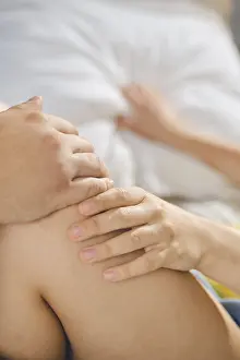 Young Adult Relationship Drucke: Two hands gently touch knee in simple indoor setting