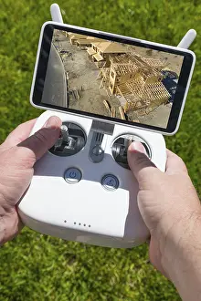 Unmanned Aerial Vehicle UAS Drucke: Hands holding drone quadcopter controller with construction house framing on screen